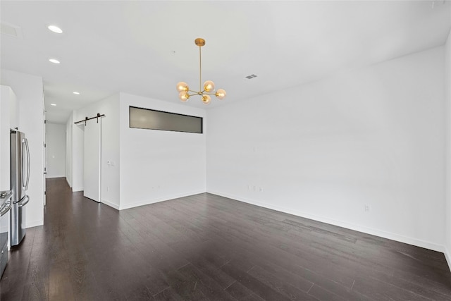 spare room featuring a chandelier, dark hardwood / wood-style floors, and a barn door