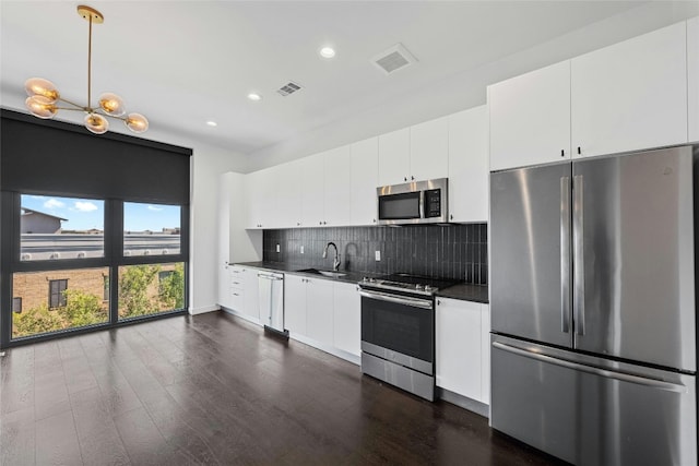 kitchen featuring dark wood-type flooring, white cabinets, hanging light fixtures, decorative backsplash, and appliances with stainless steel finishes