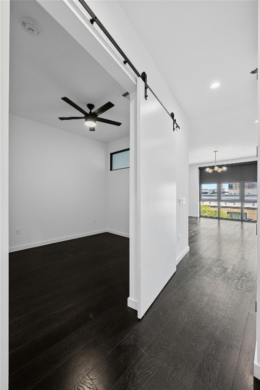 unfurnished room featuring ceiling fan with notable chandelier, dark hardwood / wood-style floors, and a barn door