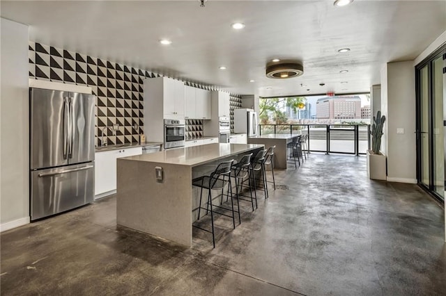 kitchen featuring expansive windows, white cabinets, appliances with stainless steel finishes, a center island, and a kitchen bar