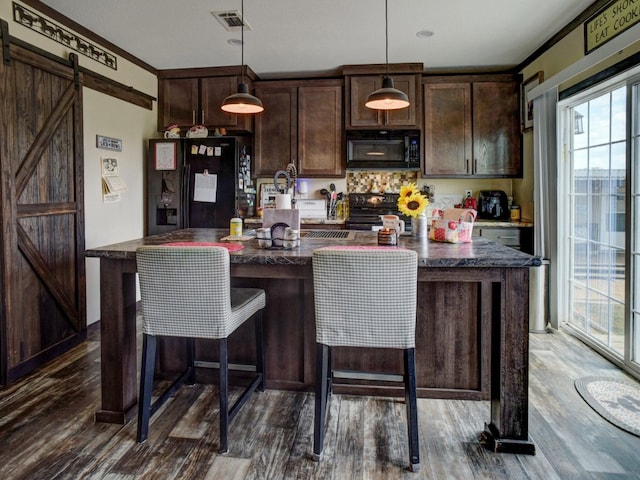 kitchen featuring dark brown cabinets, dark wood-type flooring, hanging light fixtures, a barn door, and black appliances