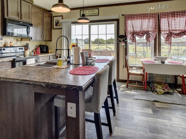 kitchen with a center island with sink, decorative light fixtures, stainless steel electric range oven, and plenty of natural light