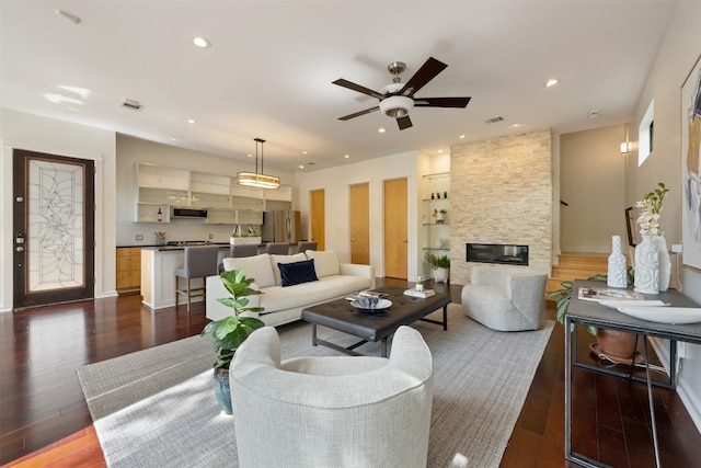 living room featuring a stone fireplace, dark hardwood / wood-style floors, and ceiling fan