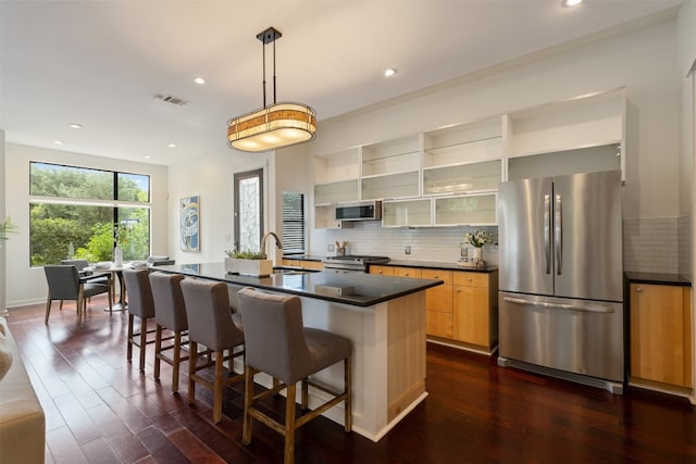 kitchen with pendant lighting, dark wood-type flooring, appliances with stainless steel finishes, an island with sink, and a kitchen bar