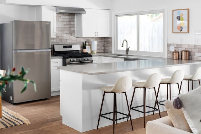 kitchen featuring sink, white cabinetry, a kitchen bar, light hardwood / wood-style flooring, and stainless steel appliances