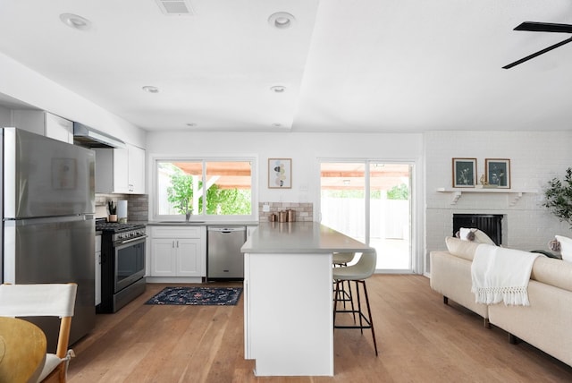 kitchen with light hardwood / wood-style floors, a breakfast bar, white cabinets, a fireplace, and stainless steel appliances