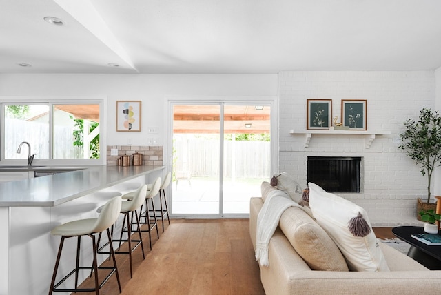 living room with light hardwood / wood-style floors, sink, and a brick fireplace