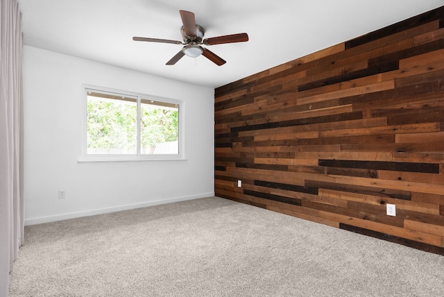 empty room with carpet flooring, wood walls, and ceiling fan