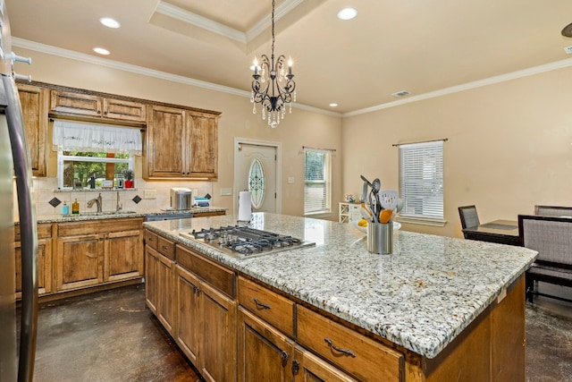 kitchen featuring a chandelier, stainless steel gas cooktop, a kitchen island, decorative backsplash, and crown molding