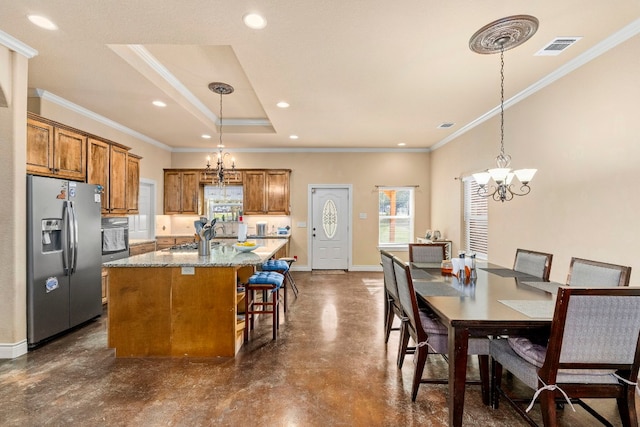 kitchen with an island with sink, ornamental molding, stainless steel appliances, and decorative light fixtures