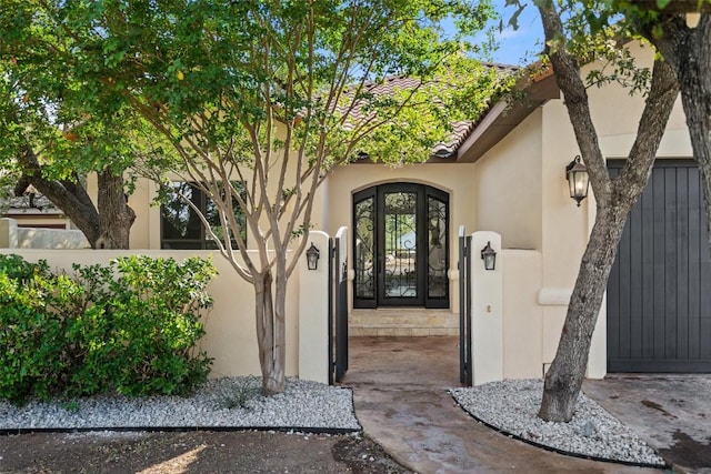 entrance to property featuring french doors, a tile roof, fence, and stucco siding