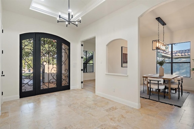 foyer featuring arched walkways, french doors, a raised ceiling, an inviting chandelier, and baseboards