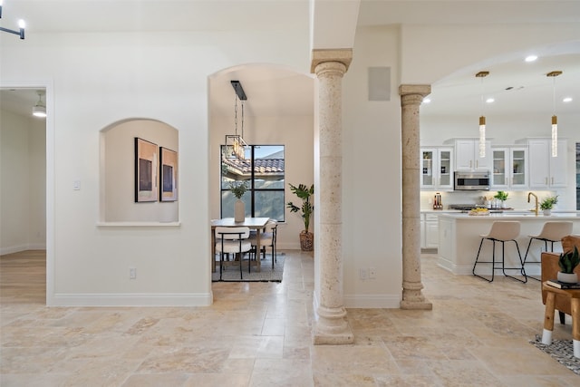 interior space with white cabinets, a kitchen bar, decorative light fixtures, and ornate columns