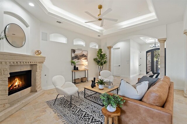 living room with a fireplace, a tray ceiling, ornate columns, and ceiling fan