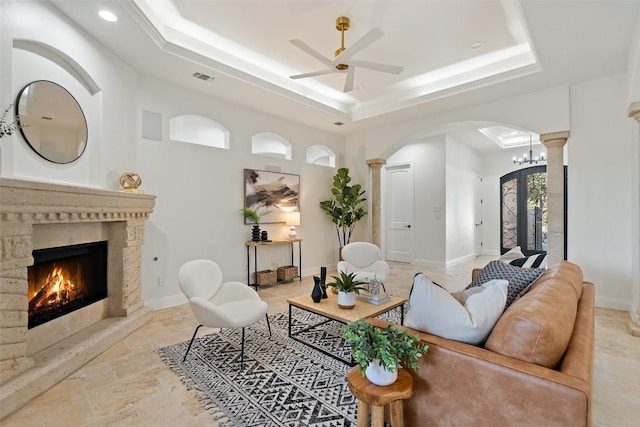 living room featuring decorative columns, a tray ceiling, arched walkways, and baseboards