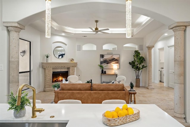 interior space featuring a tray ceiling, washer / clothes dryer, ceiling fan, a warm lit fireplace, and ornate columns