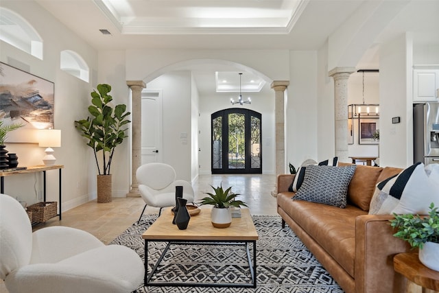 living room featuring a raised ceiling, ornate columns, and a notable chandelier