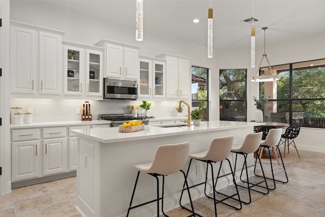 kitchen with pendant lighting, a kitchen island with sink, decorative backsplash, white cabinetry, and stainless steel appliances