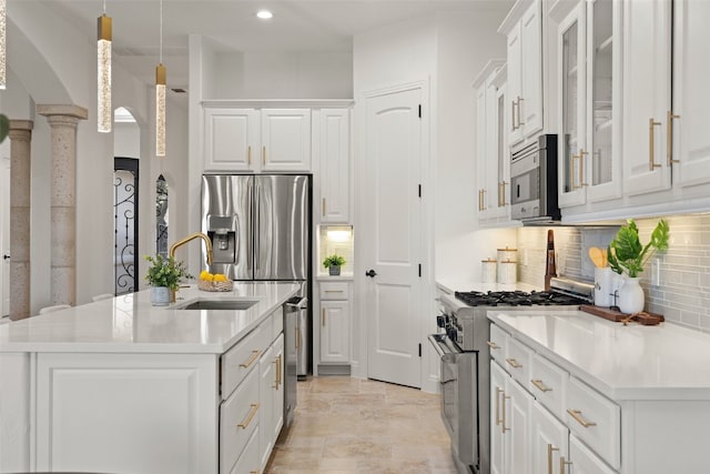 kitchen with white cabinets, a kitchen island with sink, appliances with stainless steel finishes, and decorative columns