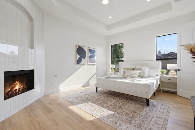 bedroom featuring light hardwood / wood-style floors, multiple windows, a tray ceiling, and ceiling fan