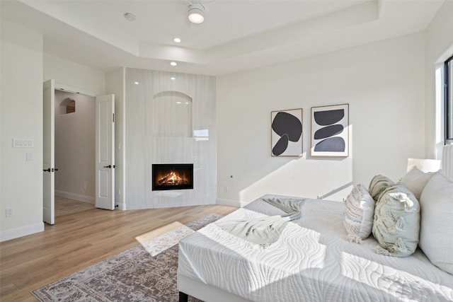 bedroom featuring light wood-style floors, a fireplace, baseboards, and a raised ceiling