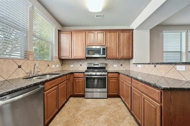 kitchen with stainless steel appliances, backsplash, dark stone countertops, and sink