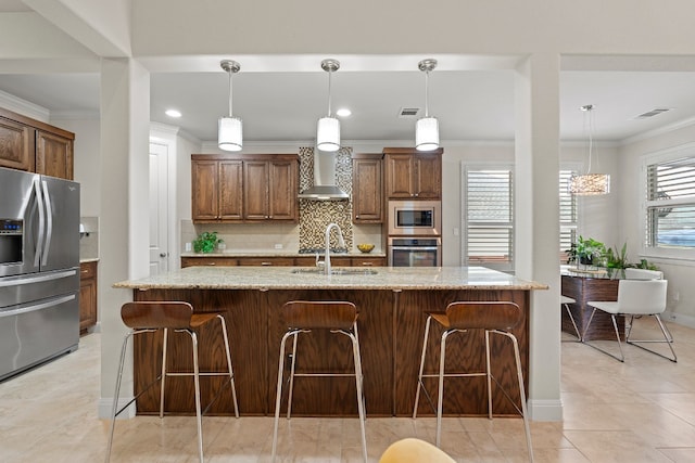 kitchen featuring stainless steel appliances, light stone countertops, an island with sink, and wall chimney exhaust hood