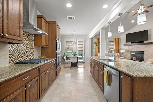 kitchen featuring wall chimney exhaust hood, a center island with sink, decorative light fixtures, sink, and appliances with stainless steel finishes