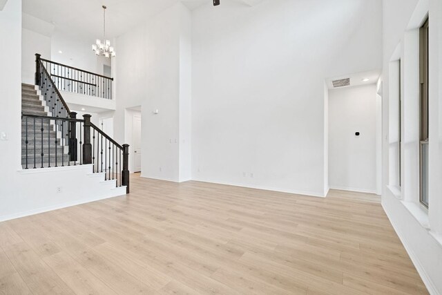 408 Ridgewell Loop, Georgetown, TX 78633 - unfurnished living room featuring stairs, a towering ceiling, light wood-style floors, a chandelier, and baseboards