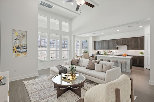 living room with ceiling fan, sink, a towering ceiling, and dark hardwood / wood-style floors