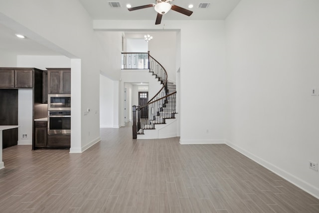 unfurnished living room featuring ceiling fan, hardwood / wood-style flooring, and a high ceiling