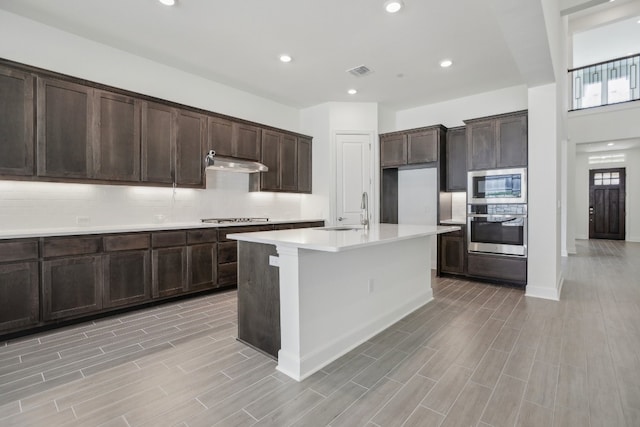 kitchen featuring dark brown cabinets, a center island with sink, light wood-type flooring, and sink