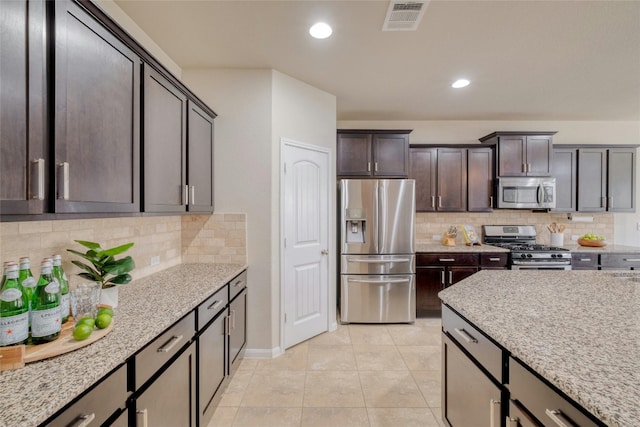 kitchen featuring decorative backsplash, appliances with stainless steel finishes, light stone counters, and dark brown cabinets