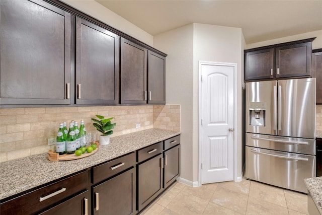 kitchen featuring backsplash, light stone countertops, stainless steel fridge with ice dispenser, dark brown cabinetry, and light tile patterned floors