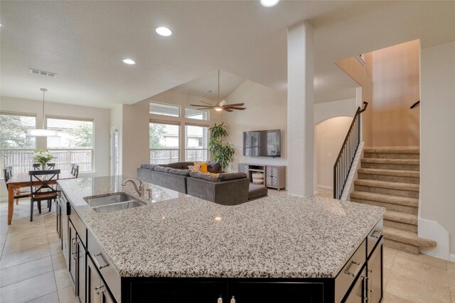 kitchen with sink, ceiling fan, light stone counters, light tile patterned floors, and a center island with sink