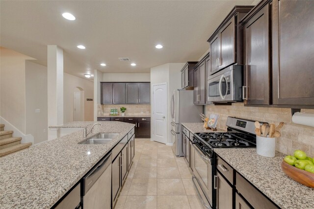 kitchen with decorative backsplash, dark brown cabinets, light stone counters, sink, and stainless steel appliances