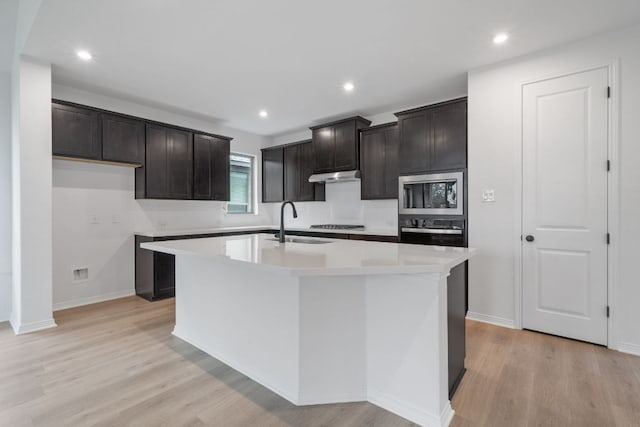 537 Raleigh Dr, Georgetown, TX 78633 - kitchen with appliances with stainless steel finishes, under cabinet range hood, an island with sink, light wood-type flooring, and light countertops