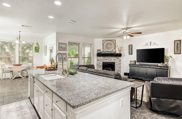 kitchen with white cabinetry, a stone fireplace, sink, a kitchen island with sink, and light stone counters