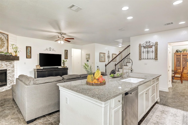 kitchen featuring a kitchen island with sink, a fireplace, stainless steel dishwasher, white cabinets, and sink