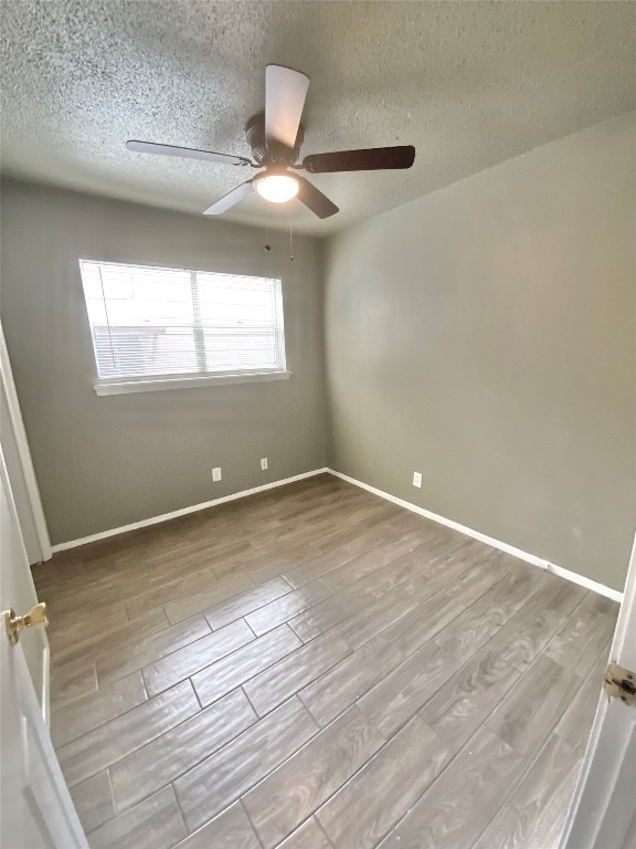 empty room featuring a textured ceiling, light wood-type flooring, and ceiling fan