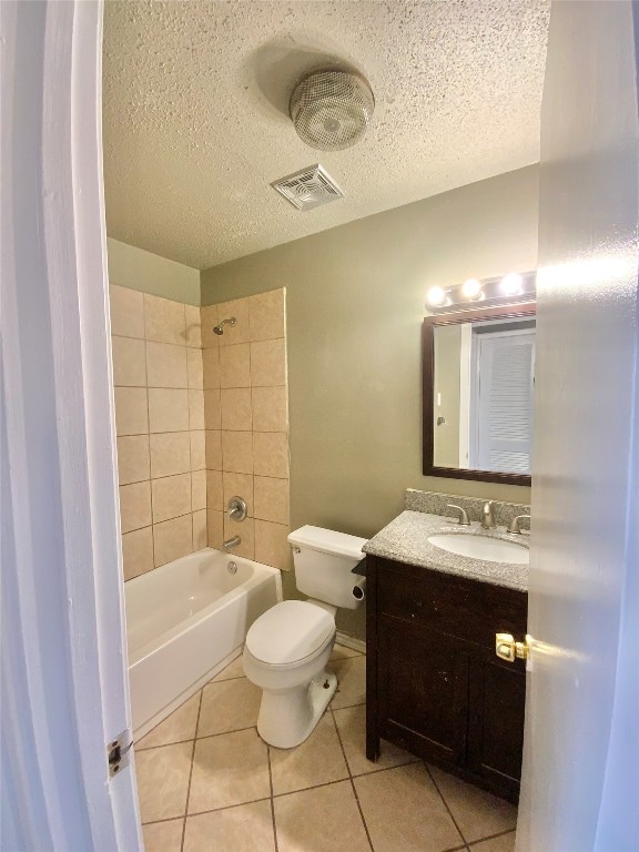 full bathroom with tile patterned floors, a textured ceiling, toilet, vanity, and tiled shower / bath