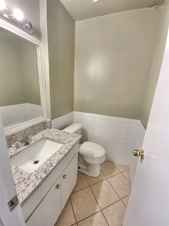 bathroom featuring tile patterned floors, a textured ceiling, toilet, vanity, and tile walls