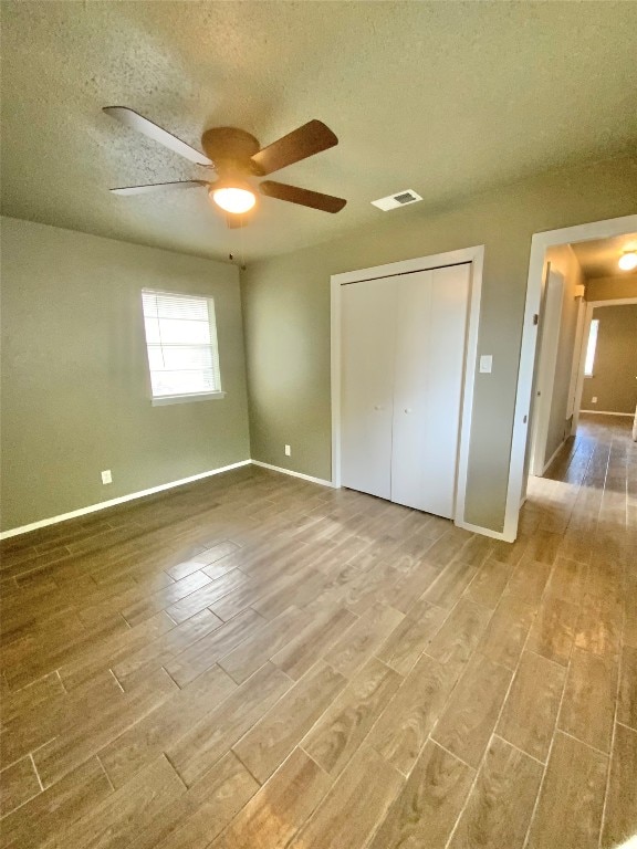 unfurnished bedroom featuring hardwood / wood-style flooring, ceiling fan, a textured ceiling, and a closet