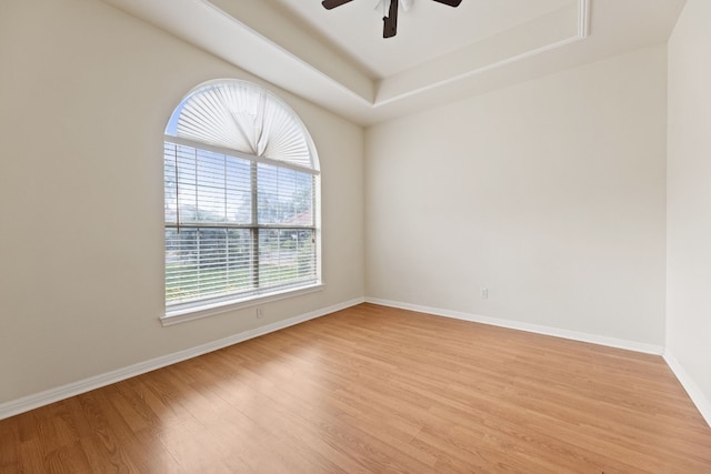 spare room featuring light wood-type flooring, a tray ceiling, and ceiling fan