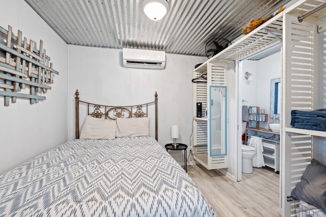 bedroom featuring ensuite bath, hardwood / wood-style floors, and an AC wall unit