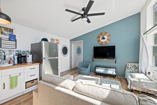 living room with light wood-type flooring, lofted ceiling, sink, and ceiling fan