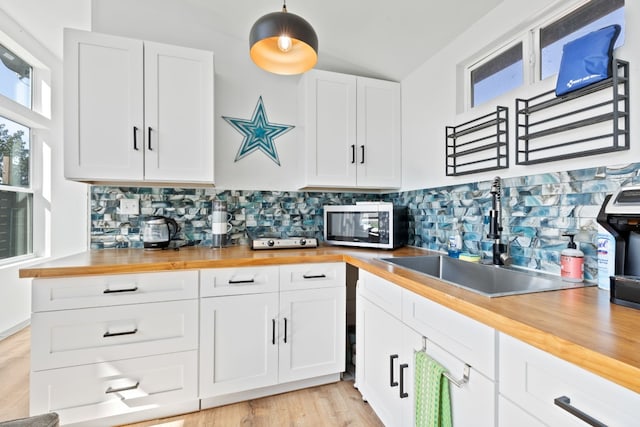 kitchen featuring hanging light fixtures, light hardwood / wood-style floors, white cabinets, wood counters, and sink