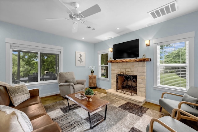 living room featuring a healthy amount of sunlight, a fireplace, ceiling fan, and light hardwood / wood-style flooring