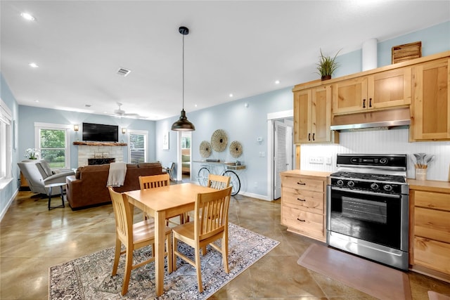 kitchen with hanging light fixtures, a stone fireplace, light brown cabinetry, ceiling fan, and stainless steel range