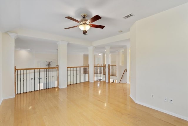 empty room featuring ornate columns, visible vents, a ceiling fan, wood finished floors, and baseboards